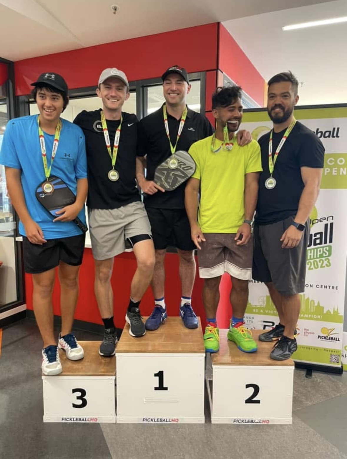 Sueme Rajpal displaying silver medal after at the 2023 Victorian Open Pickleball Championships while standing on a podium with other professional pickleball players.